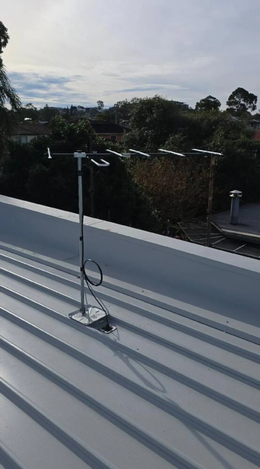 A television antenna and mast on a metal roof.