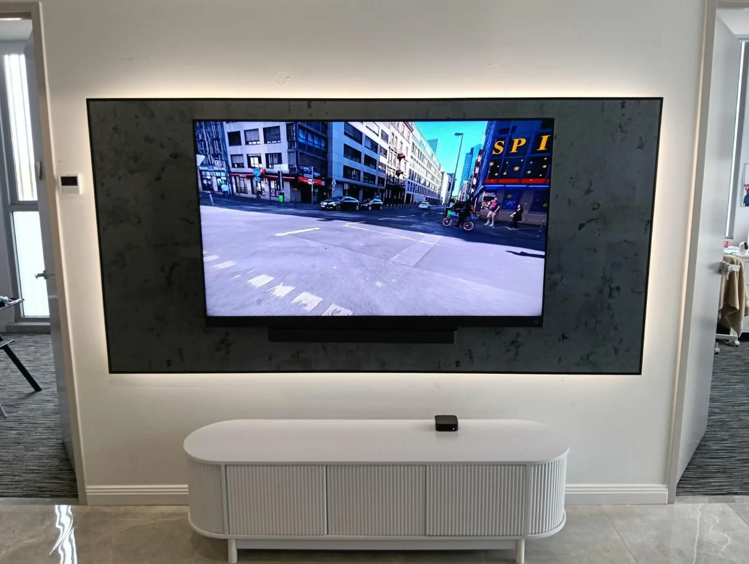 A wall-mounted television set against a dark textured panel.